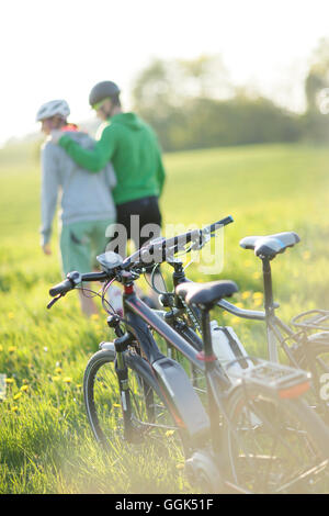 Due ciclisti con E-bikes riposa in un prato di fiori, Munsing, Alta Baviera, Germania Foto Stock