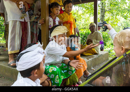 Bambini Balinese giocando con il tedesco ragazzo di 3 anni, abiti tradizionali alla cerimonia del tempio, religione Balinese, passeggino, ho Foto Stock