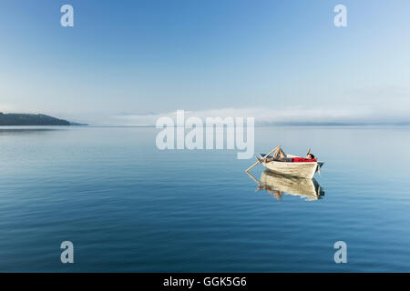 Uomo in una barca a remi sul lago di Starnberg, le Alpi e il monte Zugspitze nella nebbia mattutina, Berg, Alta Baviera, Germania Foto Stock