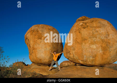 Donna in piedi tra due del round di rocce rosse chiamati Demoni marmi e fingendo di mantenerli, diavoli marmi Conservati Foto Stock