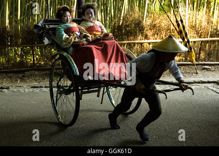 Due giovani donne geisha essere tirato attraverso una foresta di bamboo da ricksha, Kyoto, la regione di Kansai, Giappone Foto Stock