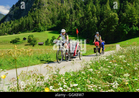 Due ciclisti con rimorchio per bambini equitazione lungo Inn percorso ciclabile, Zams, Tirolo, Austria Foto Stock