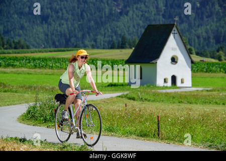 Donna in bicicletta lungo Inn percorso ciclabile, cappella in background, Karres, Tirolo, Austria Foto Stock