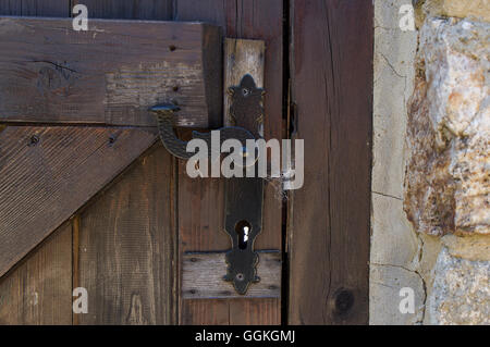 Vecchio metallo masaneta sulla porta di legno con parete fatta di pietre Foto Stock