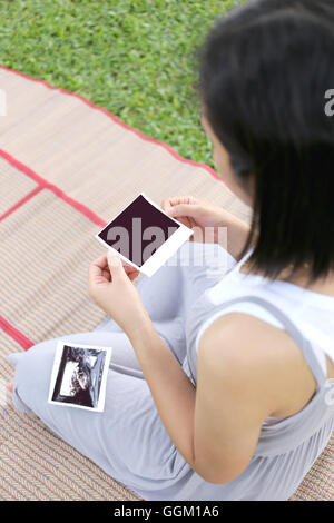 Asian Le donne in stato di gravidanza mostrano film di ultrasuoni baby picture sul suo ventre in mano a giardino. Foto Stock