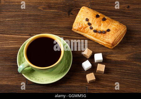 Green tazza di caffè vicino al bianco, marrone zollette di zucchero e pasta con un sorriso Foto Stock