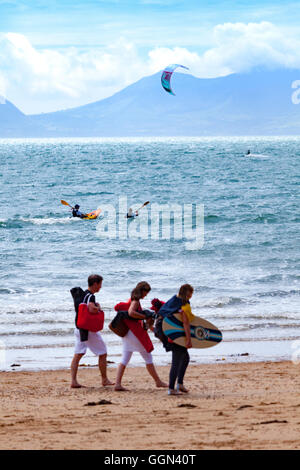 Skimboarders, canoisti e kite surfer tutti godendo di un clima caldo e il mare pulito e spiaggia di Newborough, Anglesey, Galles, Regno Unito Foto Stock