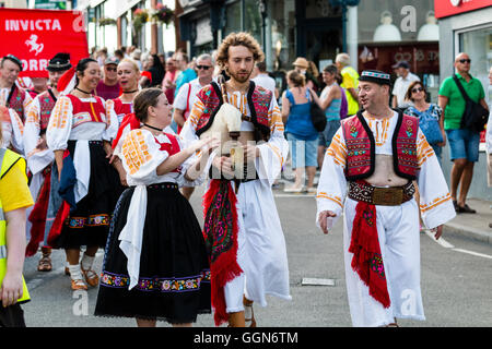 Broadstairs Settimana della Musica Folk Festival. Parade. Morena slovacca compagnia di danza artisti interpreti o esecutori in tradizionale costume slovacco, marciare lungo High Street verso il visualizzatore. Un uomo che trasportava cornamuse. Foto Stock