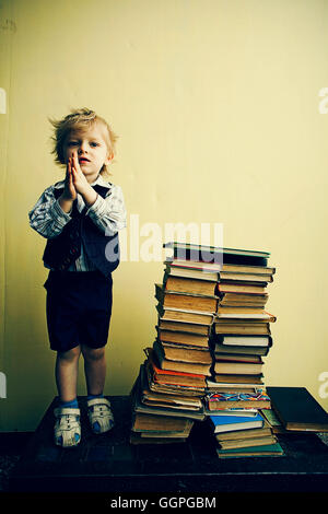Ragazzo in piedi accanto a pile di libri Foto Stock