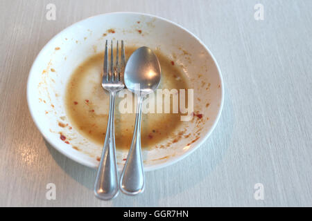 Piatto bianco sporco dopo aver messo un cibo e finito di mangiare sul tavolo del ristorante. Foto Stock