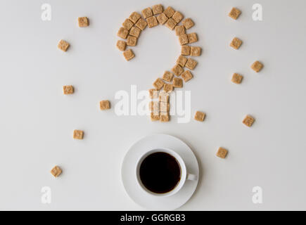 Zollette di zucchero a forma di punto interrogativo e la tazza di caffè su sfondo bianco. Vista dall'alto. Dieta dolce unhealty concetto di dipendenza Foto Stock