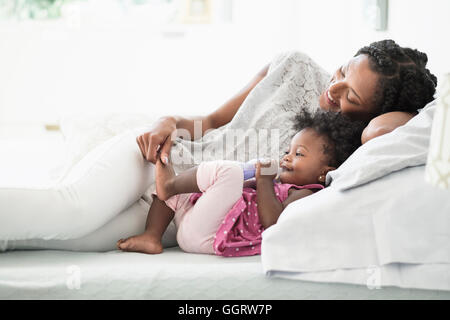 Nero donna giocando con il piede della bambina sul letto Foto Stock