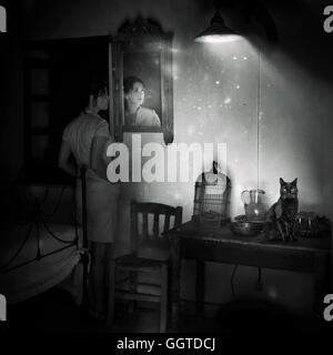 Giovane donna in piedi dallo specchio nella vecchia sala con gatto nero seduto sul tavolo Foto Stock