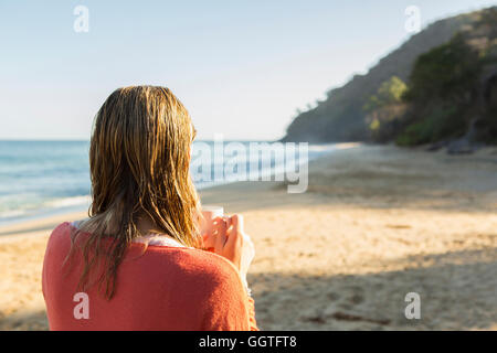 La donna caucasica di bere il caffè sulla spiaggia Foto Stock