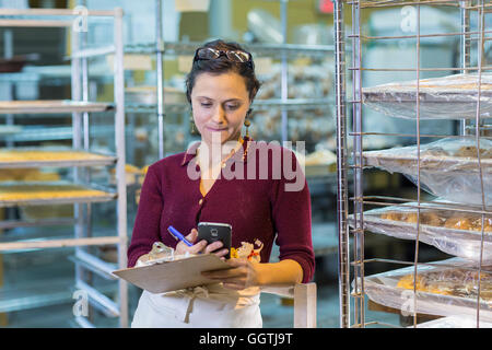 La donna caucasica holding clipboard usando il cellulare in forno Foto Stock