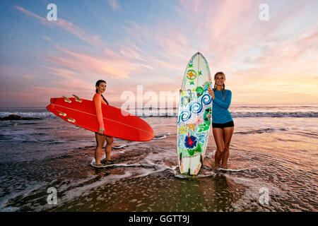 Le donne in piedi in oceano onde tenendo le tavole da surf in spiaggia Foto Stock