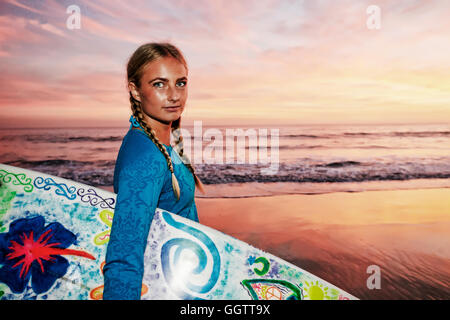 La donna caucasica che trasportano le tavole da surf in spiaggia Foto Stock
