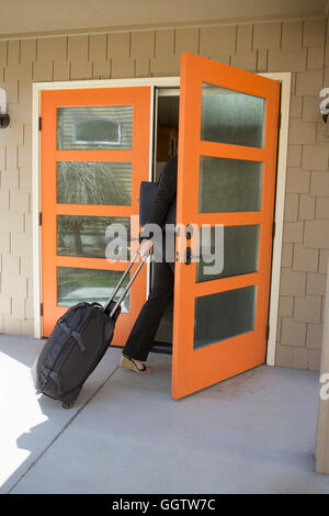 Imprenditrice tirando valigia scorrevole attraverso la porta Foto Stock