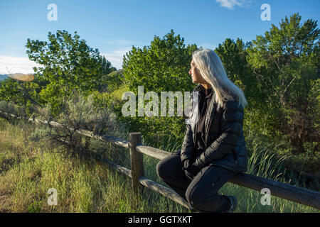 I vecchi Caucasian donna seduta sulla recinzione di legno Foto Stock