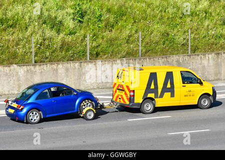 Logo vista laterale e posteriore sul business dei guasti AA gialli Furgone e conducente che trainano un'auto blu Volkswagen VW Beetle Percorrere l'autostrada M25 Essex Inghilterra UK Foto Stock