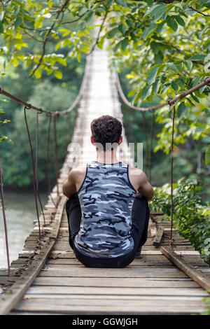 Adolescente ragazzo seduto su un ponte in legno sul fiume Foto Stock