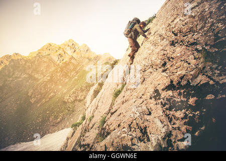 L'uomo viaggiatore con zaino grande arrampicata sulle rocce di viaggio il concetto di stile di vita paesaggio delle montagne sullo sfondo Summer Adventure ext Foto Stock