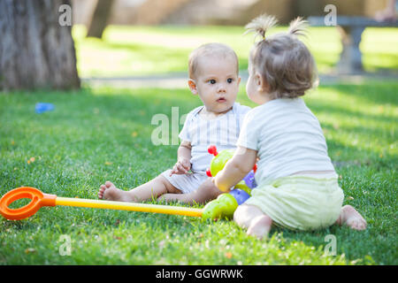 Baby boy e toddler girl giocare seduto su erba verde in posizione di parcheggio Foto Stock