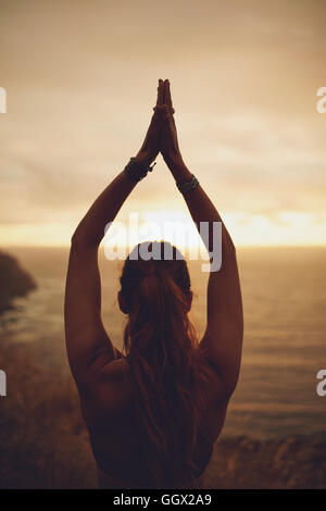 Silhouette di giovane donna sana pratica lo yoga al tramonto. Vista posteriore del fitness donna femmina con le mani giunte sopra la testa. Foto Stock