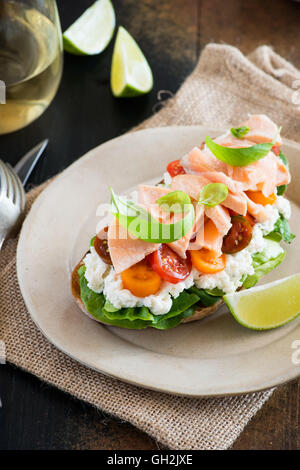 Sandwich con formaggio a pasta morbida, salmone e pomodori sulla piastra su legno rustico sfondo, vino bianco e insalata fresca sul lato, appare Select Foto Stock