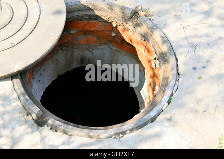 Cesspit in cemento con una botola aperta sul terreno in estate. Foto Stock