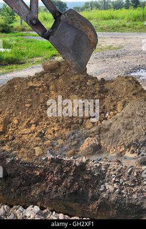 Benna di un escavatore lo scavo di una trincea nel terreno. Foto Stock