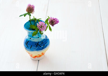 Tre fiori di trifoglio in caraffa in ceramica bianca sul tavolo di legno Foto Stock