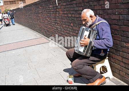 Un anziano suonatore ambulante di strada suona la fisarmonica per i soldi per le strade di Londra Foto Stock