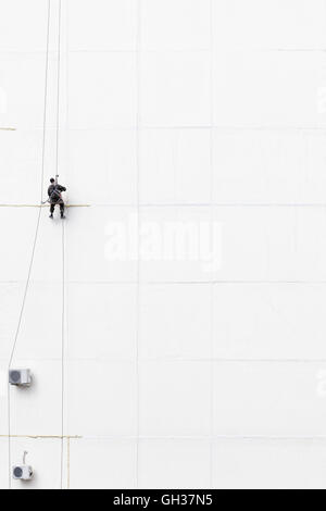 Lavoratore di manutenzione al di fuori di arrampicata su una parete Foto Stock