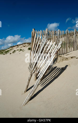 Spiaggia di sabbia, il cielo blu con un usurato staccionata in legno al centro dell'immagine, giornata di sole la recinzione getta ombre sulla spiaggia. Foto Stock