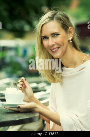 Donna bionda seduto fuori al cafe e bere cioccolata calda con panna montata Foto Stock