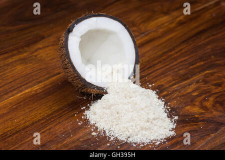 Una metà di noce di cocco con noce di cocco grattugiata riversandosi su di un tavolo di legno. Foto Stock
