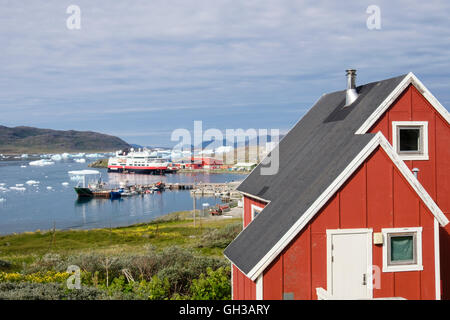 Rosso di legno casa Groenlandese affacciato sul porto di pesca nel fiordo Tunulliarfik con gli iceberg galleggianti in estate. Narsaq Groenlandia Foto Stock