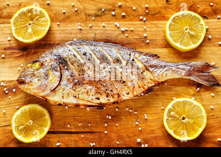 Arrosto testa dorato orate di pesce su un tavolo di legno con limoni e a grana grossa sale. Foto Stock