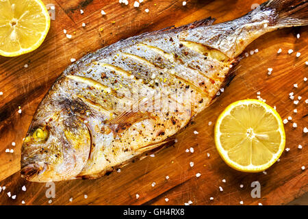 Arrosto testa dorato orate di pesce su un tavolo di legno con limoni e a grana grossa sale. Foto Stock