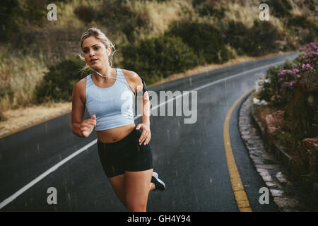 Montare la giovane donna jogging all'aperto sull'autostrada. Atleta femminile della formazione in esecuzione in un giorno di pioggia. Foto Stock