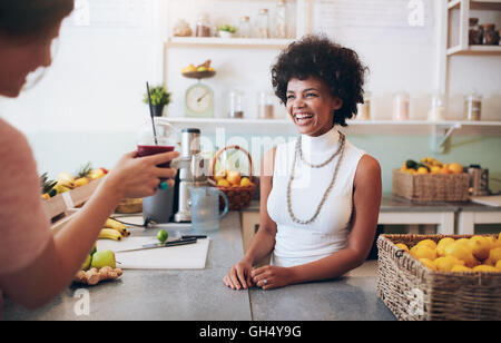 Ritratto di sorridente giovane donna africana in piedi dietro il succo di bar counter e parlare con il cliente tenendo un bicchiere di fresco jui Foto Stock