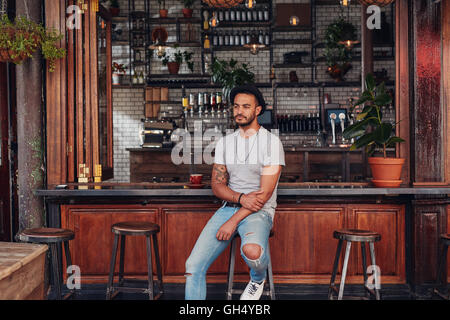 Ritratto di sconvolgere giovane uomo seduto da solo ad un cafe contatore. Moderno e giovane uomo caucasico guardando gravi. Foto Stock