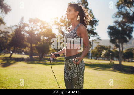 Foto all'aperto di una donna determinata che salta all'aperto in natura. esercizio fisico femminile con corda per saltare in un parco in una giornata di sole. Foto Stock