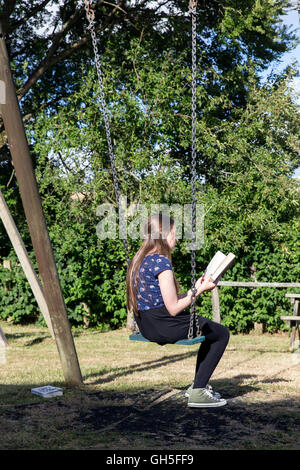 Lettura della ragazza in village park, bambino, park, nero, prati, alberi, amici, relazione, boy, anteriore, ragazza, rilassamento, lettura, relax, estate, Foto Stock