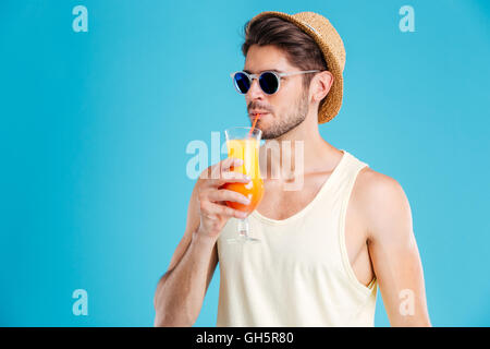 Bel giovane uomo in cappello e occhiali da sole a bere il succo d'arancia fresco Foto Stock