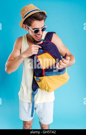 Felice giovane nel cappello e occhiali da sole aprendo il suo zaino Foto Stock