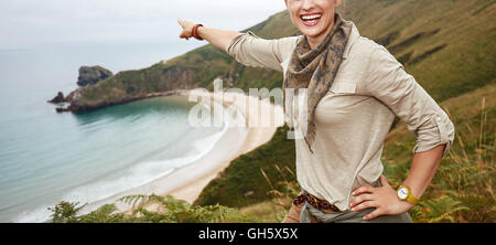 Nel selvaggio in Spagna. sorridente donna attiva escursionista puntando su qualcosa di fronte vista oceano paesaggio Foto Stock