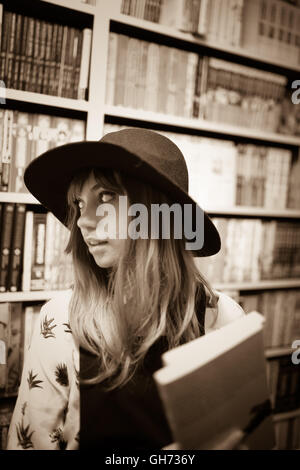 Seppia fotografia di un dodicenne bionda ragazza caucasica indossando un cappello nero in un comic book store azienda 2 Manga libri, Foto Stock