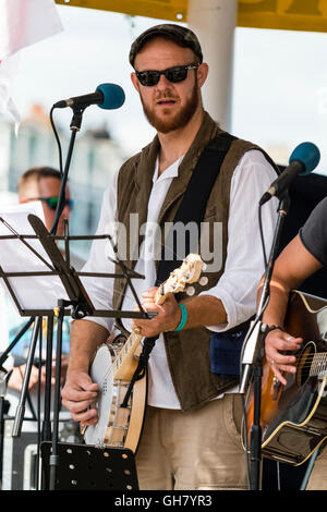 Broadstairs settimana della musica folk festival. Giovane cantante folk indossando occhiali da sole scuri, suonare il banjo di eseguire all'aperto nel palco per spettacoli. Close-up. Foto Stock